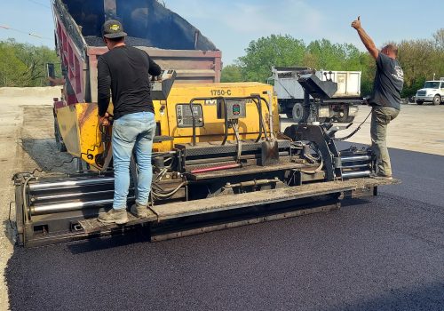 two men working on an asphalt paver machine paving a parking lot